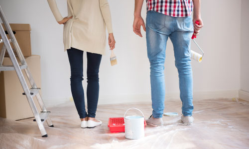 Young couple painting thw walls of their new house -DG Pinnacle Home Loans