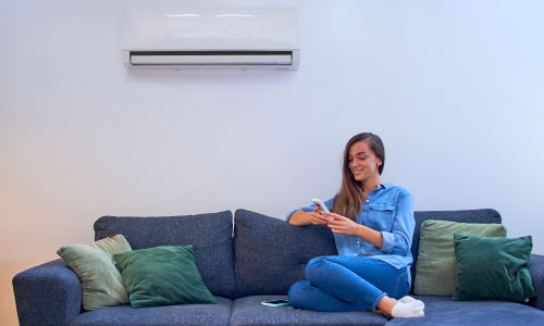 Young woman sitting on a couch under air conditioner - DG Pinnacle Home Loans