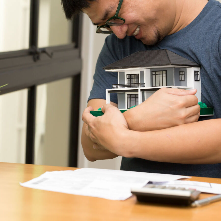 Young happy asian man hugging a model house - DG Pinnacle Home Loans - HARP Loans - Miami Mortgage Company