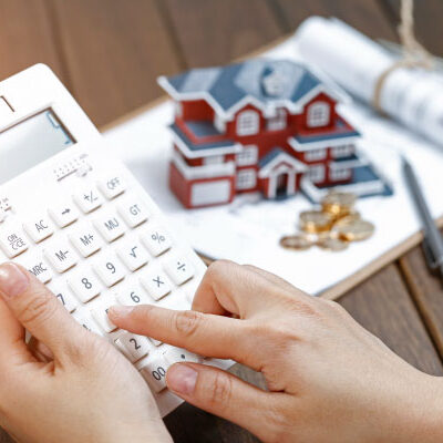 Female homebuyer calculating mortgage rates on calculator next to a small model house - DG Pinnacle Home Loans - Daily Rates - Miami Mortgage Company