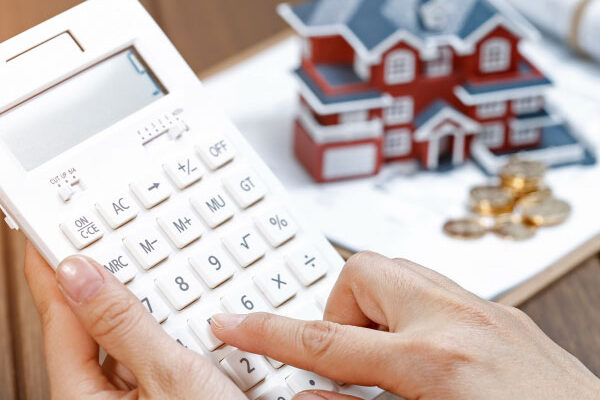 Female homebuyer calculating mortgage rates on calculator next to a small model house - DG Pinnacle Home Loans - Daily Rates - Miami Mortgage Company