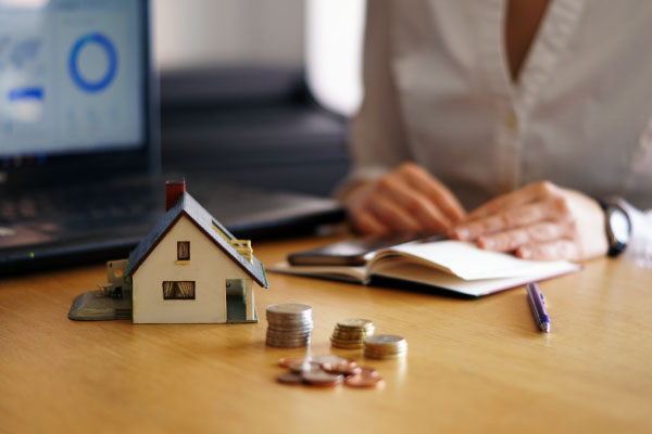 Model house and some coins on a table and a person working behind - 4 Ways to Get Approved for an FHA Loan - DG Pinnacle Home Loans - Miami Mortgage Lender