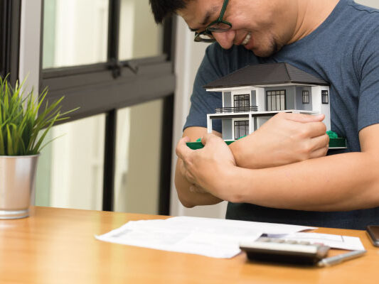 Happy young asian man hugging a model house - 5 steps for getting your mortgage pre-approved - DG Pinnacle Home Loans - Miami Mortgage Lender