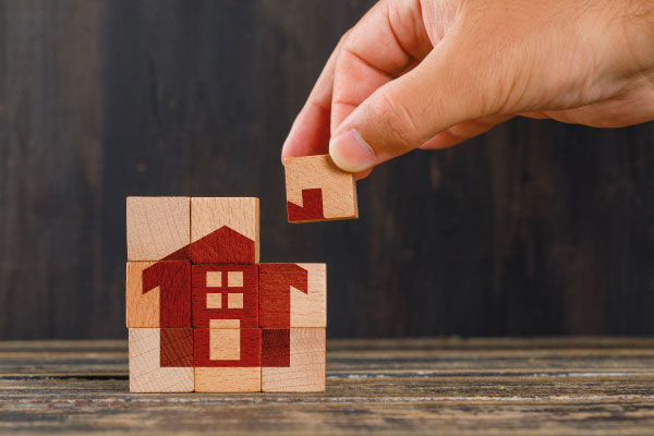 Hand setting up some wooden puzzle pieces with the printed figure of a house - The power of preapproval - DG Pinnacle Home Loans - Miami Mortgage Lender