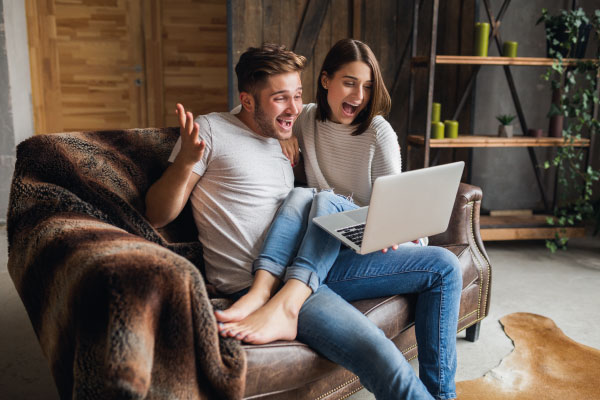 Happy young couple sitting on their couch and smiling for being preapproved - The power of preapproval - DG Pinnacle Home Loans - Miami Mortgage Lender