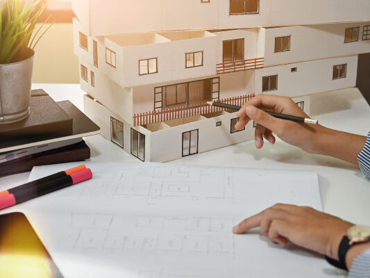 Female architect working with model house and blueprints - Who Can Become a Real Estate Investor? - DG Pinnacle Home Loans - Miami Mortgage Lender