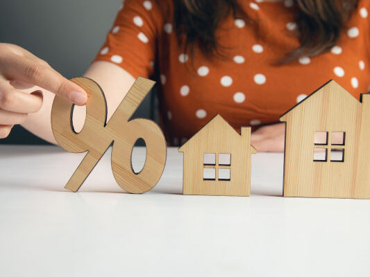 Female holding home model and wooden sale percentage sign - Home Prices Fell For First Time in 3 Years - DG Pinnacle Home Loans - Miami Mortgage Lender