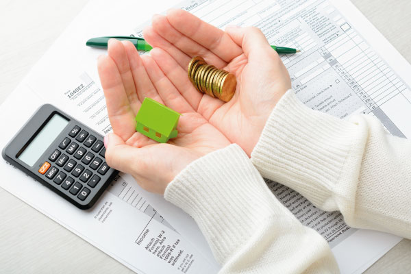 Stack of coins over model house next to tax returns calculator - Top 7 Tax Benefits of Owning a Home - DG Pinnacle Home Loans - Miami Mortgage Lender