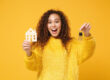 Beautiful young woman in yellow sweater holding a model house and keys | Single Women Own More Homes Than Single Men | DG Pinnacle Home Loans - Miami Mortgage Lender