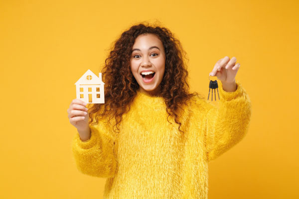 Beautiful young woman in yellow sweater holding a model house and keys | Single Women Own More Homes Than Single Men | DG Pinnacle Home Loans - Miami Mortgage Lender