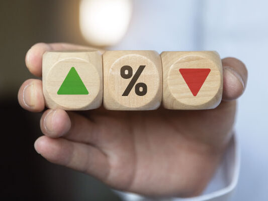 Businessman holding wooden cube blocks with percentage symbols - Will Rates Go Down in July 2023? | DG Pinnacle Home Loans | Miami Mortgage Funding Lender