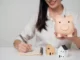 Happy woman holding piggy bank with model house | Saving for a house | DG Pinnacle Home Loans - Miami Mortgage Lender