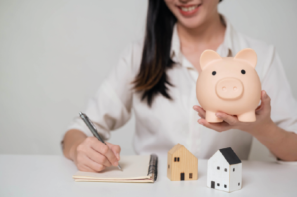 Happy woman holding piggy bank with model house | Saving for a house | DG Pinnacle Home Loans - Miami Mortgage Lender
