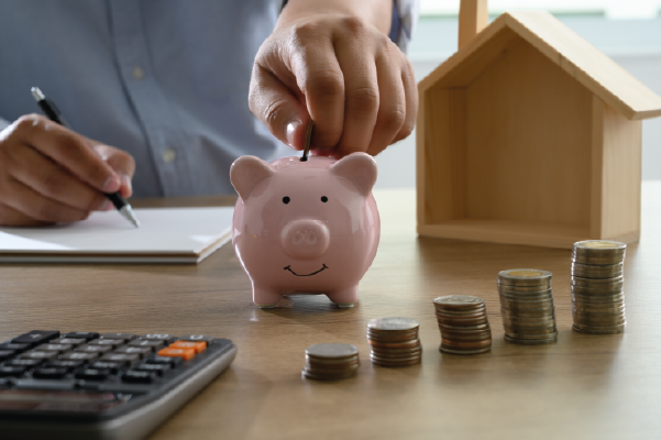 Man inserting coin in piggy bank next to model house | Saving for a house | DG Pinnacle Home Loans - Miami Mortgage Lender