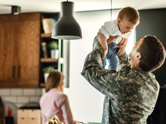 Happy baby having fun with his military dad and mom in background - VA Home Loan Benefits | DG Pinnacle Home Loans | Miami Mortgage Lender