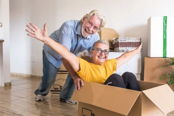 Senior couple having fun with a cardboard box | Should I Payoff My Mortgage Before I Retire? | DG Pinnacle Home Loans - Miami Mortgage Lender